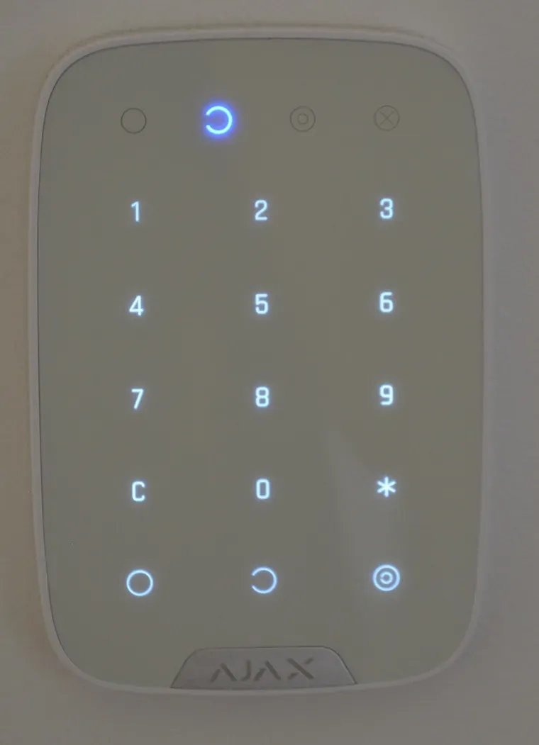 Close-up of an installed Ajax alarm keypad on a wall, with the number keys and arm and disarm buttons lit