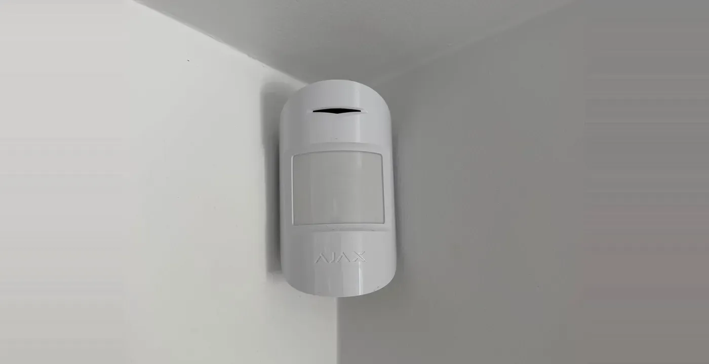 An Ajax wireless motion detector installed high in the corner of a room, below the ceiling